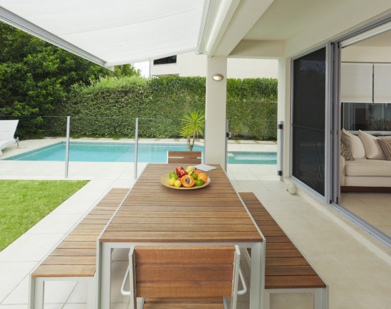 Modern suburban backyard and living room with table setting and swimming pool